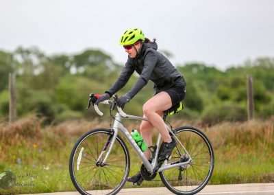 Bright yellow bike helmet with red sunglasses on female cyclist riding gravel trail.
