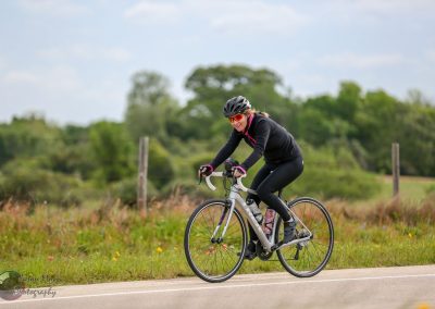 Vibrant woman cyclist riding on scenic countryside road with greenery, showcasing Bluebonnet Express biking experience.