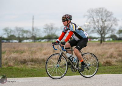 Cyclist riding on a paved trail with trees and parked cars in the background, promoting Bluebonnet Express cycling event.