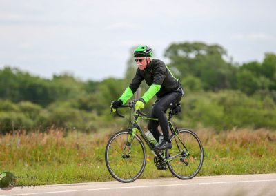 VINTAGE BICYCLE RIDER IN GREEN AND BLACK GEAR CYCLING ON COUNTRY ROAD.