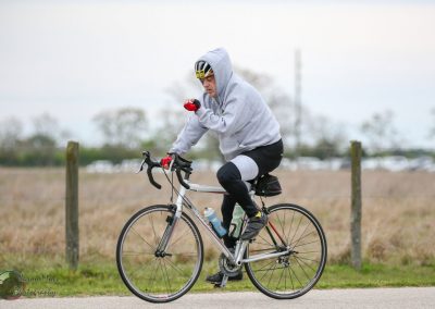 Cyclist on a road bike during a ride, wearing a hoodie and cycling gear, in a scenic outdoor setting.