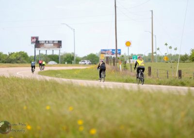 Bicycle riders enjoying a scenic ride along a rural Texas highway, promoting Bluebonnet Express cycling routes.
