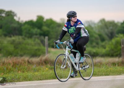 Bike rider wearing Bluebonnet Express jersey cycling outdoors in a rural setting.