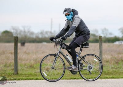 Bright cyclist equipped with face mask riding a Trek electric bike in open countryside.