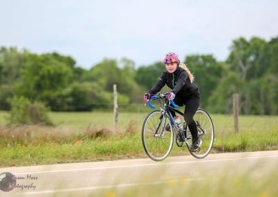 Bright female cyclist riding a road bike on a rural bike trail during daytime.