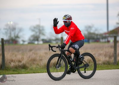 Wearing a red riding jacket, cyclist waves while riding a black bike on a scenic outdoor trail.