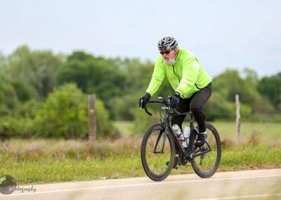 Bright green cyclist helmet and jacket on Black Bicycles during Bluebonnet Express ride in scenic countryside.