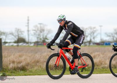 Bright orange bicycle on nature trail with cyclist in sports gear, promoting Bluebonnet Express cycling event.