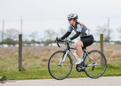 Cyclist riding a road bike outdoors with scenic background, promoting Bluebonnet Express cycling event.