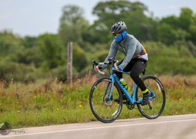 Bright blue road bike on the Bluebonnet Express cycling route in Texas, with rider in protective gear.