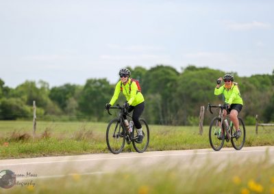 Bright yellow cycling jackets with helmets on biking women on a scenic trail.