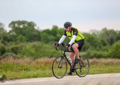 Bright yellow cyclist jersey riding a black bike on a rural road outdoor.