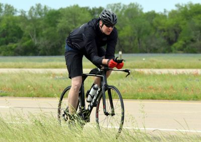 Cyclist riding on a paved trail in a scenic, grassy area during daytime.