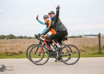 Bright female cyclists smiling and waving on tandem bicycles during outdoor ride.