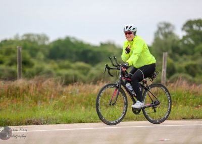 Vibrant woman cyclist in bright yellow jacket riding a road bike on rural route.