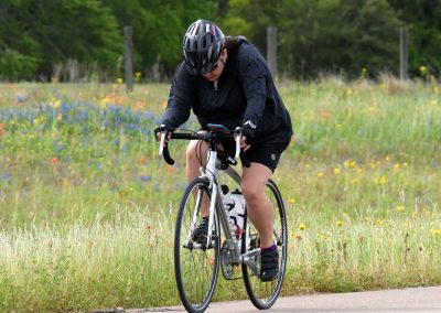 Bright female cyclist on a scenic trail with wildflowers, wearing helmet and athletic gear.