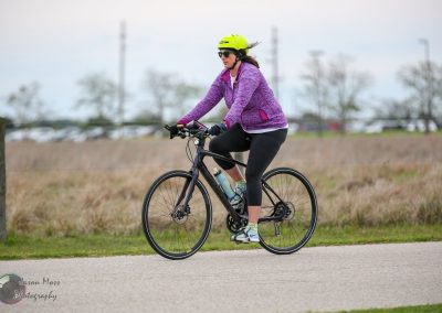 Woman riding a mountain bike on a paved trail in open countryside, outdoor activity in nature.