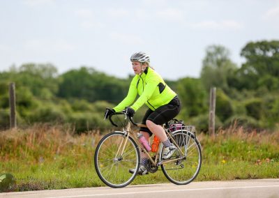 Bright yellow cycling jacket on woman riding bike along scenic rural trail.