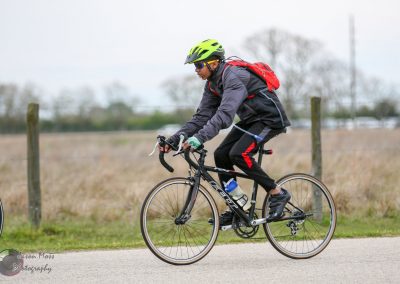 Bright yellow helmet with blue sunglasses on cyclist riding a black bicycle outdoors.