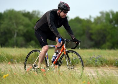 Vivid outdoor scene of a cyclist riding a Trek bike through a grassy field with wildflowers on a clear day.
