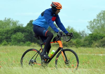 Vibrant cyclist riding a mountain bike through a grassy field with wildflowers and lush trees.