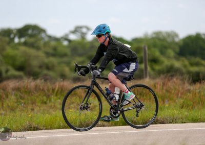 Cyclist riding a mountain bike on a scenic trail with greenery and open skies behind.