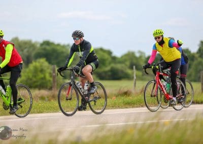 Brightly dressed cyclists riding on a scenic outdoor trail with green fields, promoting Bluebonnet Express bike tours and events.