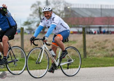 Bright male cyclist riding a road bike outdoors during a cycling event, supporting Bluebonnet Express.