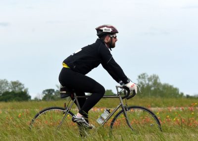 Man cycling on a bike through a grassy field, wearing a helmet and sunglasses.