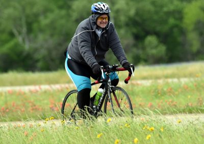 Vibrant cyclist riding through grassy field on Bluebonnet Express trail filled with flowers.