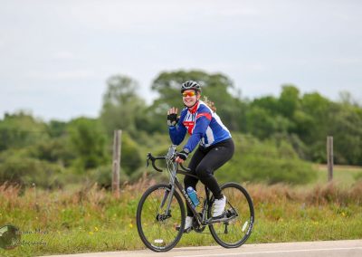 Vibrant cyclist riding a Bluebonnet Express themed bike on scenic rural road during daytime.