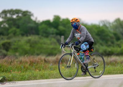 Bright cyclist riding in protective gear on a rural road during daytime.