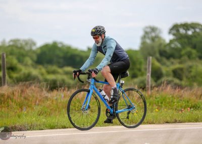 Vibrant blue bicycle on scenic outdoor ride with a mature cyclist in protective gear on a rural trail.