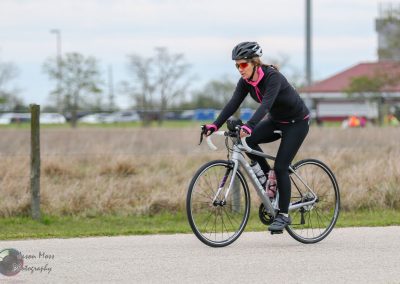 Brightly colored woman cycling outdoors with Bluebonnet Express logo, enjoying scenic Texas countryside.