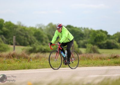 Bright green cycling jacket on man riding a road bike along scenic countryside.
