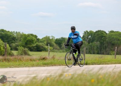 Vegan cyclist riding on a scenic rural road during daytime, promoting Bluebonnet Express.