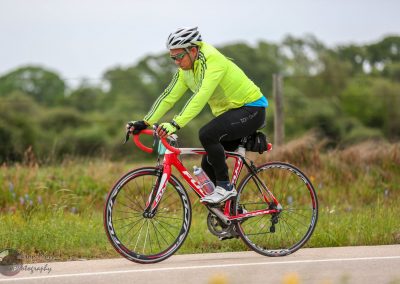 High-performance cyclist on a road bike during daytime outdoor ride, wearing a bright yellow jacket and helmet.