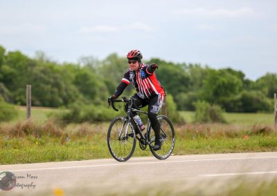 Bright cyclist riding on rural road wearing patriotic USA-themed cycling jersey and helmet.