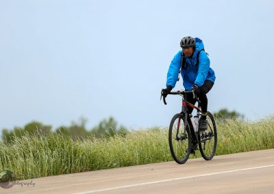 Bright blue cycling jacket and black helmet worn by cyclist riding on rural trail during daytime.