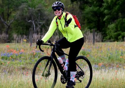 Vibrant cyclist in bright yellow jacket riding through meadow with wildflowers, promoting Bluebonnet Express biking adventures.
