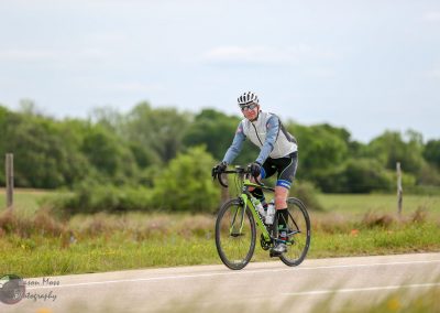 Vibrant cyclist riding on scenic outdoor bike trail with lush greenery, promoting Bluebonnet Express bike tours.
