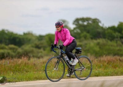 Bright pink cycling jacket woman riding road bike on nature trail for Bluebonnet Express.