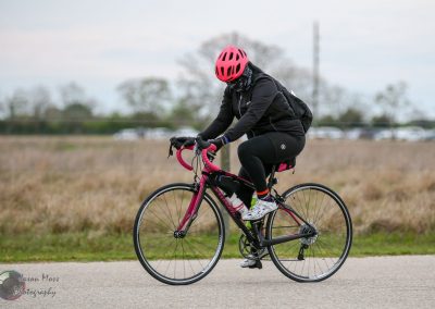 Bright pink bike helmet and accessories on a cyclist riding a road bike outdoors.