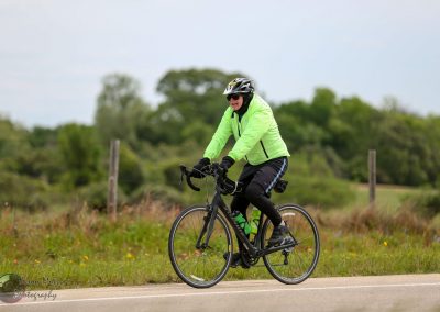 Vibrant cyclist in a neon green jacket riding on a country road surrounded by greenery.
