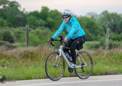 Bright blue cycling jacket on woman riding a bike on scenic trail for Bluebonnet Express.