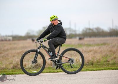 Bright green helmet worn by smiling kid riding mountain bike on paved trail in outdoors.