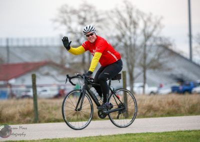 1. Experienced cyclist waving on a black road bike during outdoor ride.