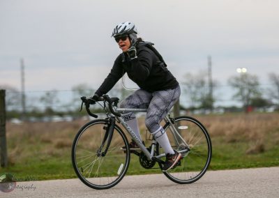 Bright woman riding a bike with helmet and sunglasses on a trail during daytime.