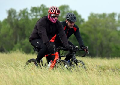 Velo riders in costume crossing a grassy field during daytime.