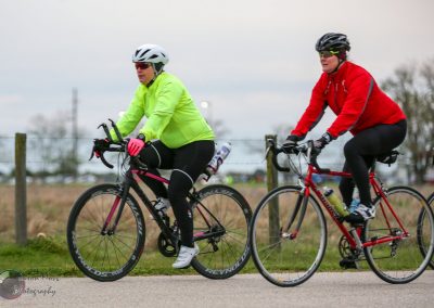 Brightly colored cyclists riding on a scenic outdoor bike trail during daytime.